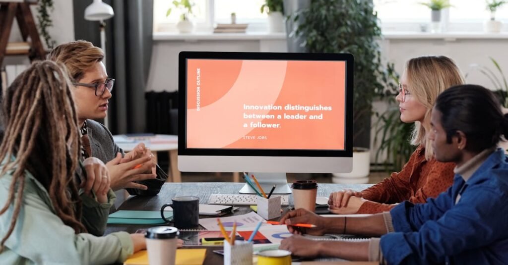 A multicultural team collaborating in an office, discussing a project with a visible monitor.